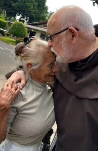 Friar Hugging Elderly Woman